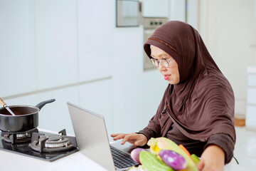 Happy smiling asian older muslim woman looking at a laptop computer