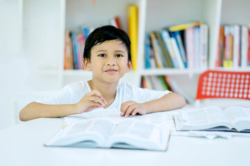 Asian boy reading a book in the library with bookshelf background