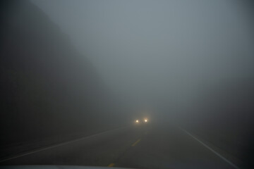 The car was passing through a foggy road, only the lights could be seen.