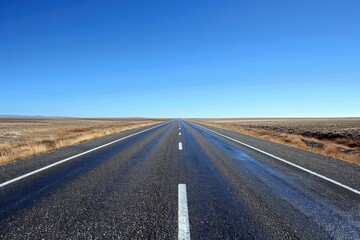 Endless highway stretching through the vast and desolate landscape, disappearing into the distant horizon under the clear blue sky.