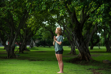 A young girl, with blond curly hair, folds her hands in namaste, meditates and thanks God, in the...