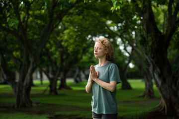 A young girl, with blond curly hair, folds her hands in namaste, meditates and thanks God, in the...