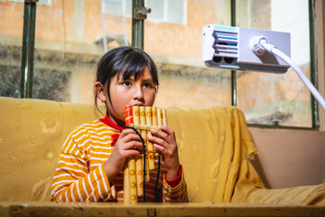 latin girl learning to play the panpipes through online classes with her cell phone - education concept