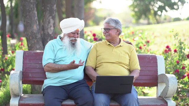 Two happy indian senior sikh punjab men friends using laptop having fun outdoor in park. Technology, internet, Retired old people,
