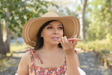 Woman recording audio on cell phone wearing sun hat. Outdoor portrait, sunny day.