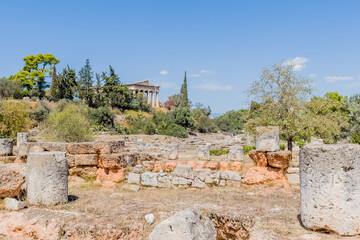 Sunny view of ancient ruins with a distant view of Hephaistos temple surrounded by lush greenery, in Athens, Greece