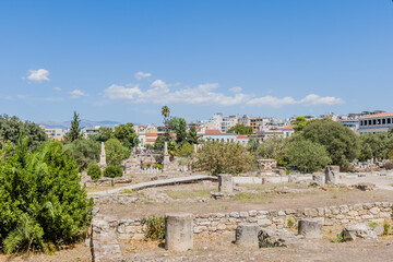 Ancient ruins in a field with a modern city and clear blue sky in the background, in Athens, Greece