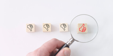 The hand makes a thumbs up on wooden cubes under a magnifying glass.