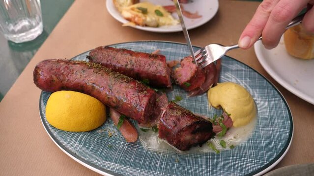Closeup slicing eating Greek traditional sausage on a plate at street taverna restaurant table in Athens