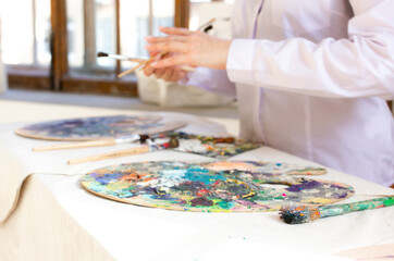 Oil color palette and brush in woman hand. Female artist painting process in studio, bright...