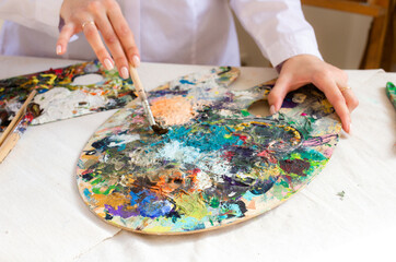Oil color palette and brush in woman hand. Female artist painting process in studio, bright...