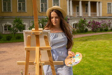 Female artist portrait painting in spring lilac garden. Woman in hat with wooden easel and canvas...