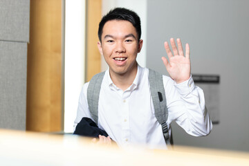 A business student with a backpack is waving towards the camera in a classroom