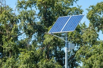 Lamp post with solar panel system on road with blue sky and trees. Autonomous street lighting using...