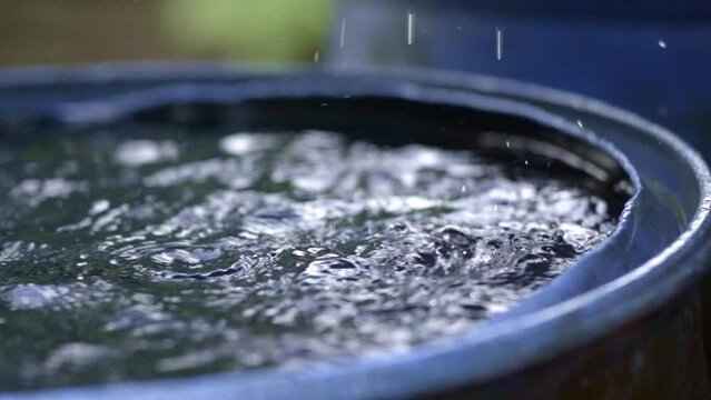 Rain drops filling up rainwater harvesting barrel, closeup slow motion