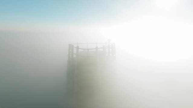 Aerial footage of a skyscraper engulfed in thick morning clouds. Illuminated by intense backlit sunshine, it captures a cinematic cityscape. LuPa Creative