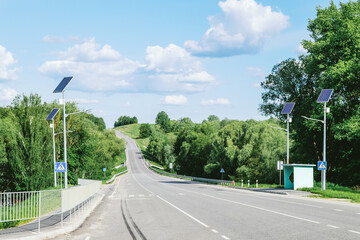 Fototapeta na wymiar Lamp post with solar panel system on road with blue sky and trees. Autonomous street lighting using solar panels. Street lamp, on batteries from the sun. Alternative renewable energy systems