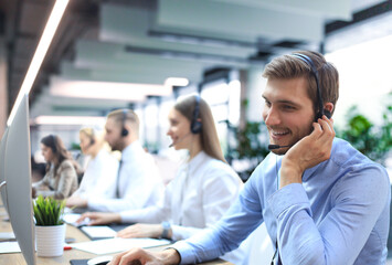 Portrait of call center worker accompanied by his team. Smiling customer support operator at work. - 785936607
