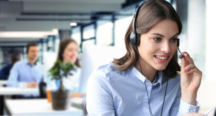 Female customer support operator with headset and smiling, with collegues at background. - 785936627