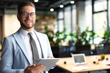 Modern business man in formalwear using digital tablet while standing near window in the office - 785936693