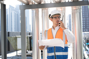 Portrait Asia male engineer in protective workwear is performing a conducts system check with use paperwork and walkie talkie at rooftop building	