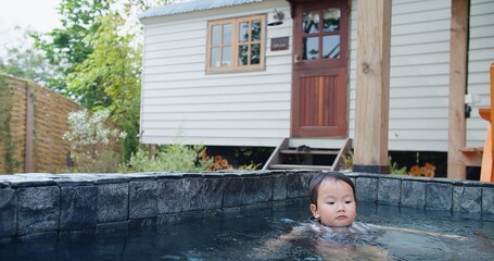 A little Asian child girl swimming in a pool of water and a house is in the background. Scene is peaceful and relaxing