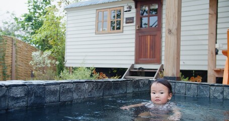 A little Asian child girl swimming in a pool of water and a house is in the background. Scene is peaceful and relaxing