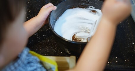 A child is making a homemade dessert chocolate cake with a parent. The child is holding a spoon...