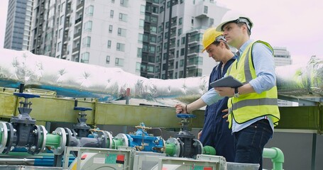 Two engineers with hard hats are checking the gauge on a pipeline valve in an urban industrial