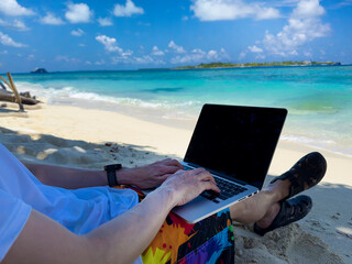 Nomad digital  young man with the laptop and running remotely with bright scenic view near poolside on the beach in summer time.