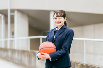 校舎の前でバスケットボールを持つ女子中学生・女子高生（部活・スポーツ・運動部・バスケ部）
