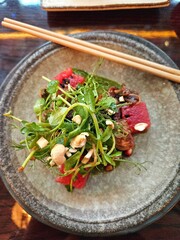 Bowl of a salad with assorted meats, veggies, and herbs, served with chopsticks