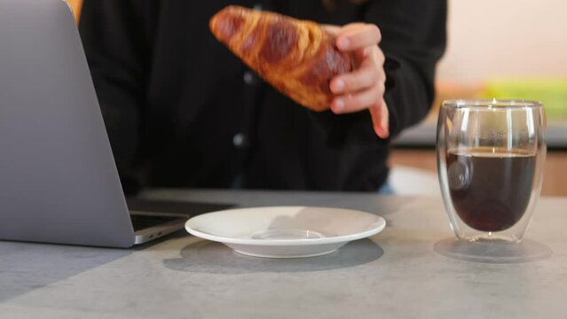 Close up video of young woman eating croissant for breakfast in kitchen.