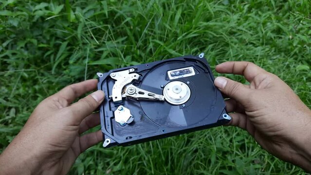 A computer technician shows a damaged hard disk against a background of green grass. Broken hard disk on green grass background
