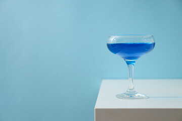 Blue drink in cocktail glass on blue background, space for text