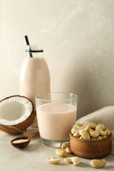 Glass and bottle with alternative milk, coconut and nuts on beige background