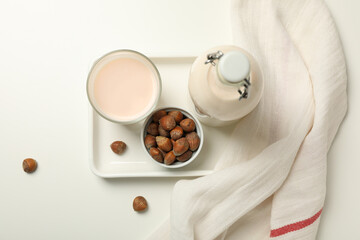 Bottle and glass with milk, towel and bowl with nuts on white background, top view