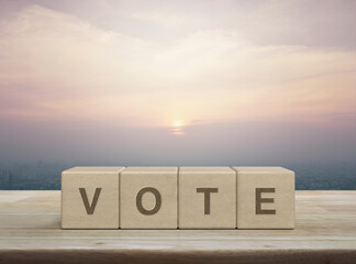 Vote letter on wood block cubes on wooden table over city tower and skyscraper at sunset, vintage style, Election and voting concept
