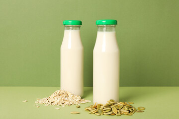 Bottles of alternative milk, pumpkin seeds and oatmeal on green background