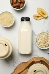 Bottle of alternative milk, herbal ingredients and paper cups on light background, top view