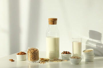 Bottle and glass with alternative milk and herbal ingredients in bowls on light background
