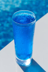 A glass of delicious blue cocktail Blue Lagoon on the background of the pool. Alcoholic cocktail juicy fruit blue with curacao liqueur, ice cubes, vertical