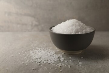 Fototapeta na wymiar Natural salt in bowl on grey textured table, space for text