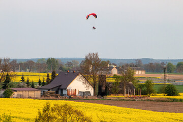 Scenic view of people paragliding over yellow fields of flowers and houses in the countryside