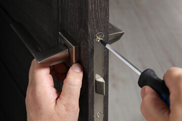 Handyman with screwdriver repairing door handle indoors, closeup