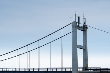 Closeup view of a suspension bridge pillar with cable line set for transportation cross in a calm blue sky during daylight
