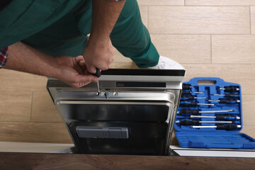 Serviceman repairing dishwasher's door with screwdriver indoors, closeup