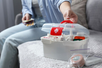 Woman holding pills indoors, focus on first aid kit