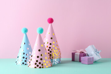 Party hats and gift boxes on color background