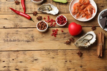 Natural aphrodisiac. Different food products and heart model on wooden table, flat lay. Space for...